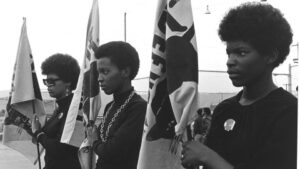Three women wearing black hold Black Panther Party flags