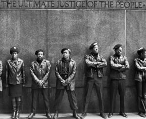 Black Panther Party members in all black, wearing berets, stand under the worlds "The Ultimate Justice of the People"