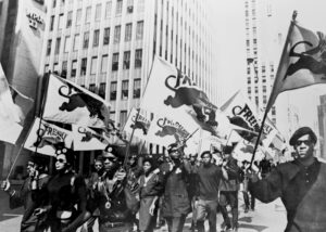 Black and white image of protesters marching and carrying Black Panther flags