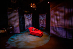 A red chaise lounge on a low-lit stage.