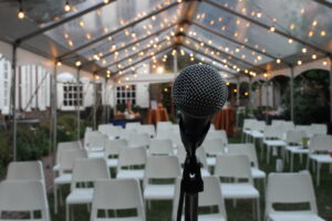 A microphone set up in front of rows of white chairs under a tent with lights