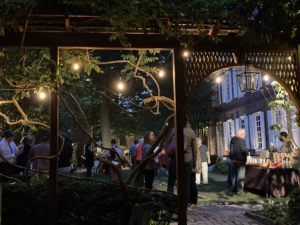 A group of people mingle in a garden with cafe lights at night
