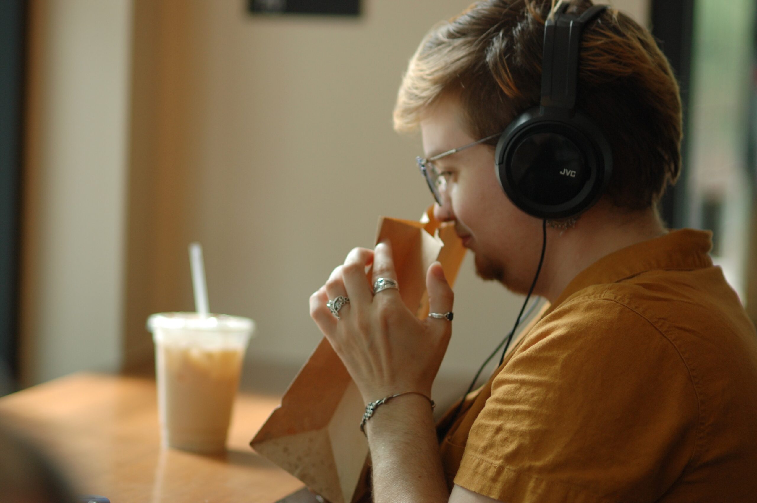 A person sits at a cafe wearing headphones and smells the aroma from a bag of coffee beans