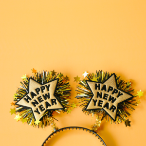 A headband with two springing gold stars with "Happy New Year" on them on a yellow background.