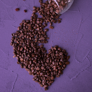 Coffee beans make the shape of a heart on a purple background.