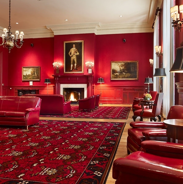 A stately red room with a painted portrait, couches, and chairs